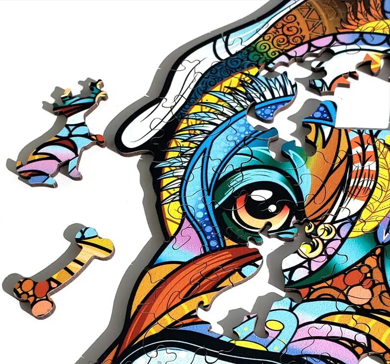 Puede incluir: Un colorido rompecabezas de madera con un dise&ntilde;o de perro estilizado. Las piezas del rompecabezas est&aacute;n intrincadamente cortadas y presentan vibrantes tonos de azul, naranja, amarillo y rosa. Se ven dos piezas sueltas, un perro y un hueso.