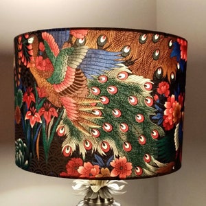 May include: A table lamp with a pineapple-shaped base and a lampshade featuring a colorful peacock design. The lampshade is made of fabric and has a black background with red, green, blue, and gold accents.