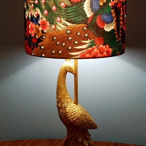 May include: A gold peacock lamp with a lampshade featuring a colorful peacock design with red, green, and blue accents. The lampshade has a floral pattern with pink and yellow flowers.