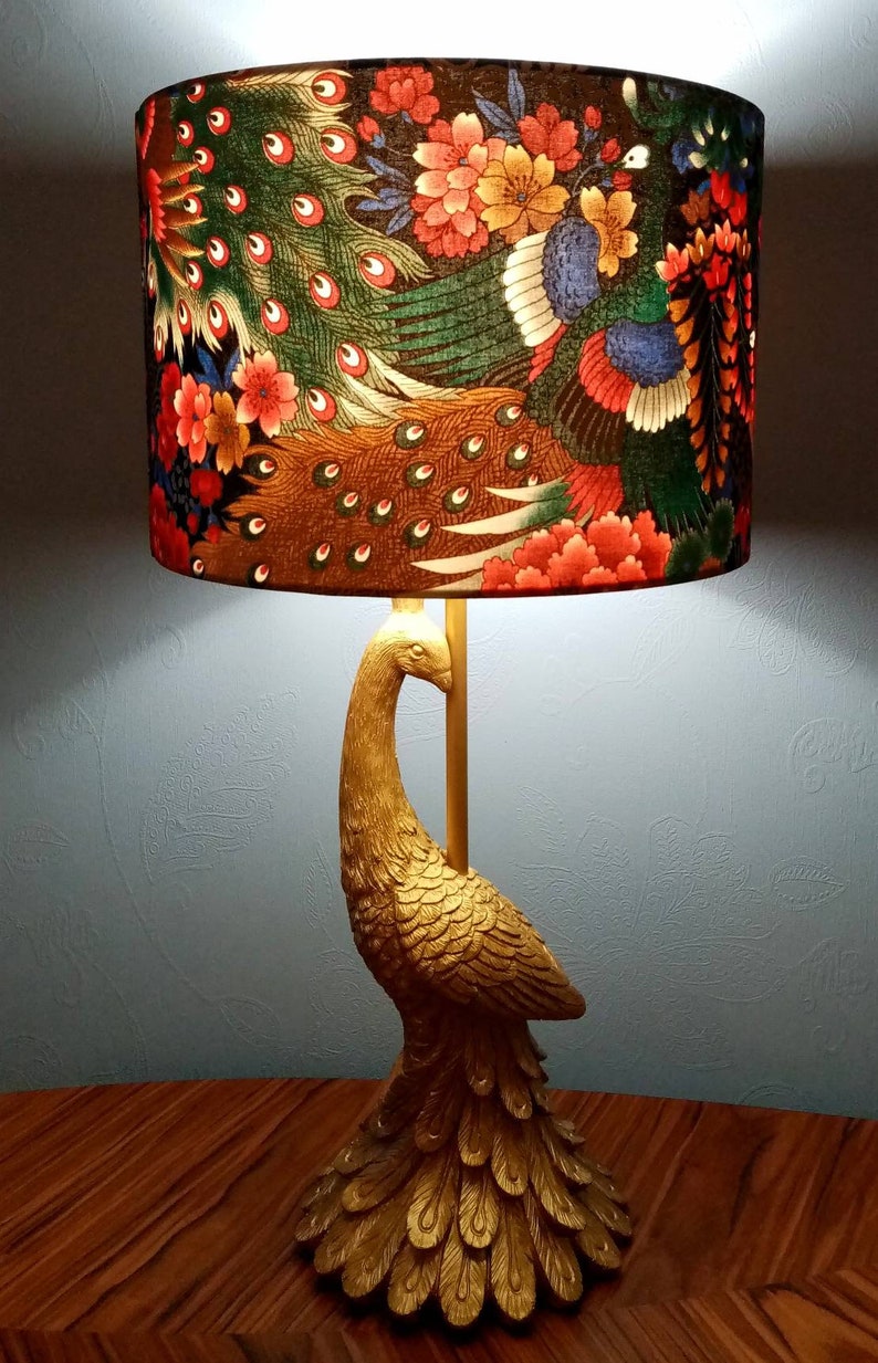 May include: A gold peacock lamp with a lampshade featuring a colorful peacock design with red, green, and blue accents. The lampshade has a floral pattern with pink and yellow flowers.
