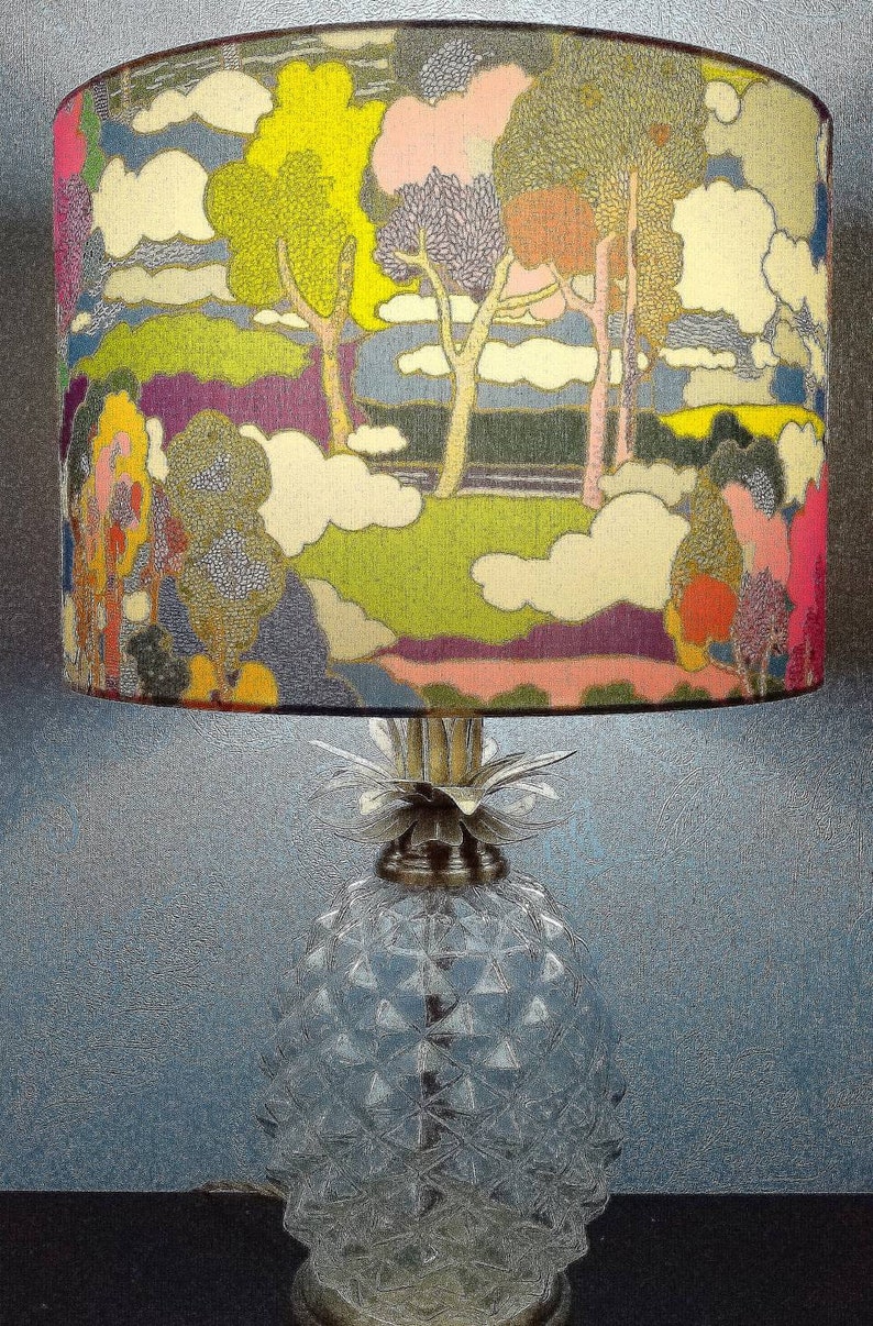 Pode incluir: Uma base de l&acirc;mpada de vidro em forma de abacaxi com um abajur colorido que apresenta uma paisagem estilizada com &aacute;rvores, nuvens e um esquema de cores rosa, verde e roxo.
