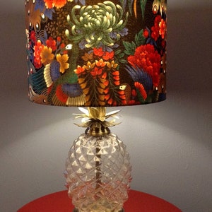 May include: A table lamp with a clear glass pineapple-shaped base and a fabric lampshade with a floral pattern in shades of red, green, gold, and black.