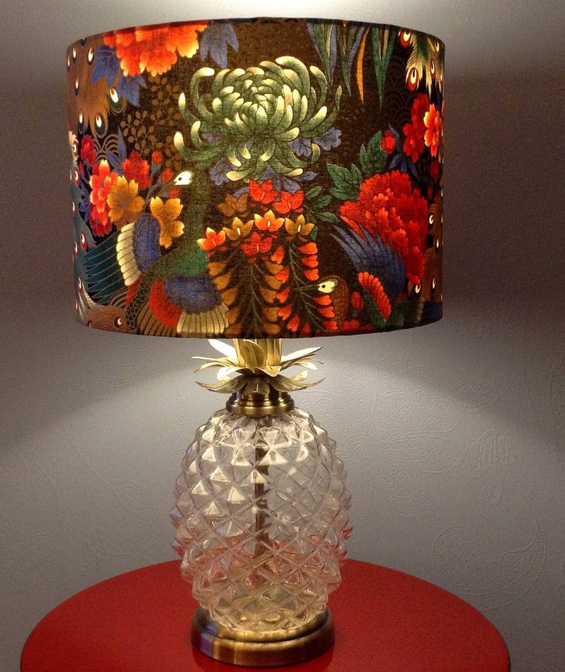 May include: A table lamp with a clear glass pineapple-shaped base and a fabric lampshade with a floral pattern in shades of red, green, gold, and black.