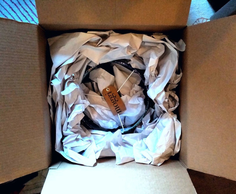 May include: A brown cardboard box with a white paper packing material inside. The packing material is crumpled and has a brown tag with the word "Moooi" written on it.