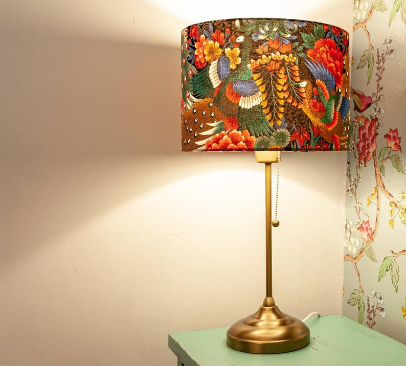 May include: A gold table lamp with a fabric lampshade featuring a colorful floral and bird design. The lampshade has a brown background with red, orange, yellow, green, and blue flowers and birds.