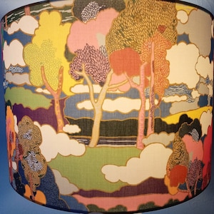 Pode incluir: Um abajur colorido com um design caprichoso que apresenta &aacute;rvores, nuvens e uma paisagem. O tecido &eacute; estampado com uma variedade de cores, incluindo rosa, amarelo, azul e verde.