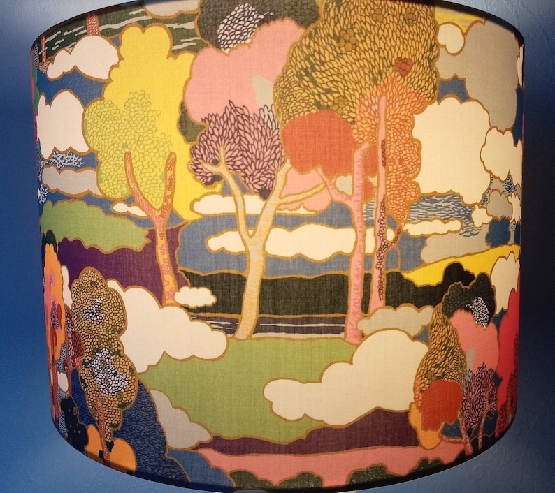 Pode incluir: Um abajur colorido com um design caprichoso que apresenta &aacute;rvores, nuvens e uma paisagem. O tecido &eacute; estampado com uma variedade de cores, incluindo rosa, amarelo, azul e verde.