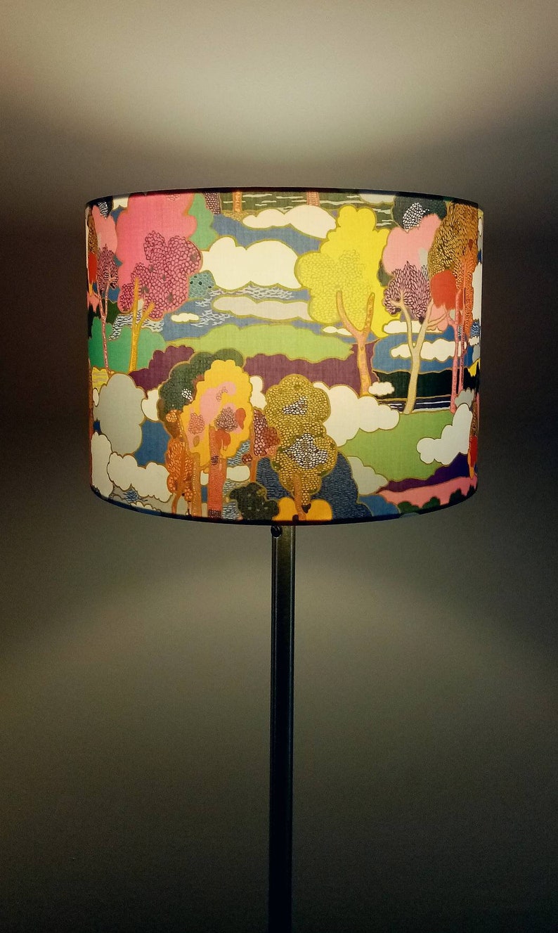Pode incluir: Um abajur colorido com uma cena de floresta caprichosa que apresenta &aacute;rvores, nuvens e um rio. O abajur &eacute; feito de tecido e tem um fundo branco com uma variedade de cores, incluindo rosa, amarelo, verde, azul e roxo.