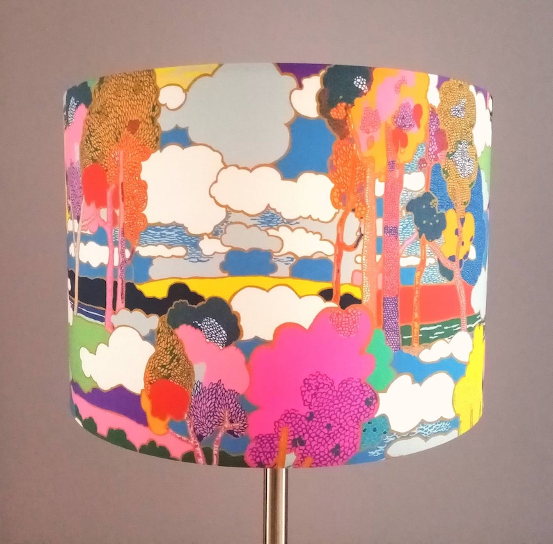 Pode incluir: Um abajur colorido com um design caprichoso que apresenta &aacute;rvores, nuvens e uma paisagem. O abajur &eacute; feito de tecido e tem uma paleta de cores brilhantes e vibrantes.