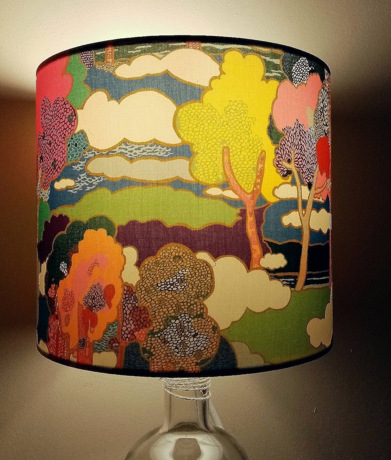 Pode incluir: Um abajur com um design abstrato colorido que apresenta &aacute;rvores, nuvens e uma paisagem. O abajur &eacute; feito de tecido e tem uma borda preta.