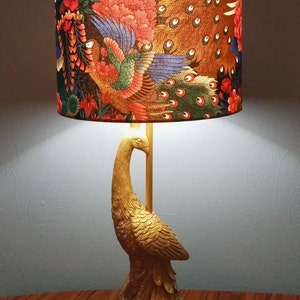 May include: A gold peacock lamp with a lampshade featuring a peacock design in shades of blue, green, red, and brown.