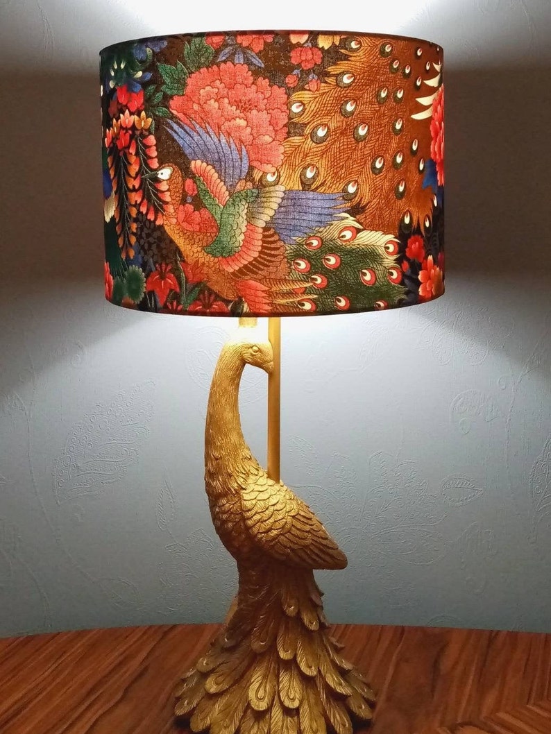 May include: A gold peacock lamp with a lampshade featuring a peacock design in shades of blue, green, red, and brown.