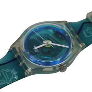 Könnte beinhalten: Eine transparente Armbanduhr aus Kunststoff mit blauem Zifferblatt und türkisfarbenem Armband. Das Armband hat ein weißes Design mit einem Gebäude und den Worten "Settecolli" und "Citypass".