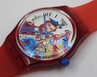 Peut inclure: Montre Swatch rouge avec un cadran blanc et une image de dessin animé d'un homme jouant de la cornemuse. Le cadran de la montre indique "Musical Off" et porte le logo Swatch.