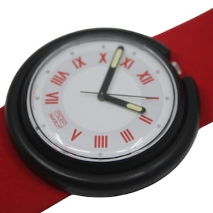 May include: A Swatch Pop watch with a white face, black bezel, and red band. The watch face features red Roman numerals and black hands. The band is a solid red color.
