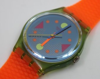 Könnte beinhalten: Eine grün-orange Swatch-Uhr mit blauem Zifferblatt und bunten geometrischen Mustern. Die Uhr hat ein Armband aus Kunststoff.