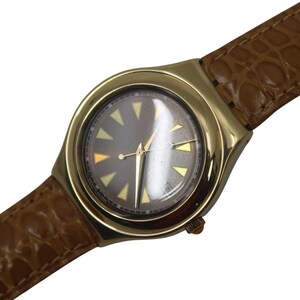 May include: A gold-toned wristwatch with a brown leather band. The watch face is gray with gold triangular markers and gold hands. The band has a textured, crocodile-like pattern.