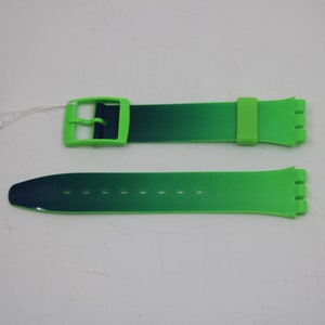 Può includere: Un cinturino per orologio in silicone con sfumatura verde e blu con una fibbia verde. Il cinturino è etichettato "G2216" e "Plus 4".