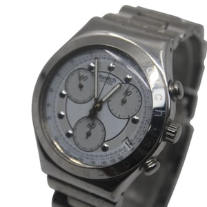May include: A silver-toned Swatch Swiss chronograph watch with a white face. The watch features three sub-dials, a date display, and a stainless steel band. The watch face has the text "swatch swiss".