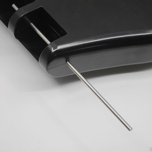 Peut inclure: Gros plan sur un remontoir de montre en plastique noir avec une tige en métal argenté qui s'étend sur le côté.