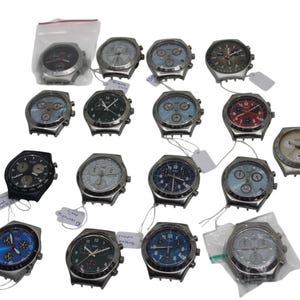 May include: A collection of various wristwatches with silver-toned cases and different colored faces, including black, blue, red, and white. Some watches are in plastic bags, and many have attached tags. The watches have multiple dials and buttons.