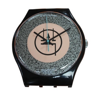 May include: A black Swatch watch with a silver face and a black and white graphic design. The watch has a black band and a silver buckle.