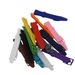 May include: A collection of silicone watch straps in a variety of solid colors including white, brown, black, green, yellow, red, orange, pink, dark blue, gray, purple, and light blue. Each strap features a buckle and multiple adjustment holes.