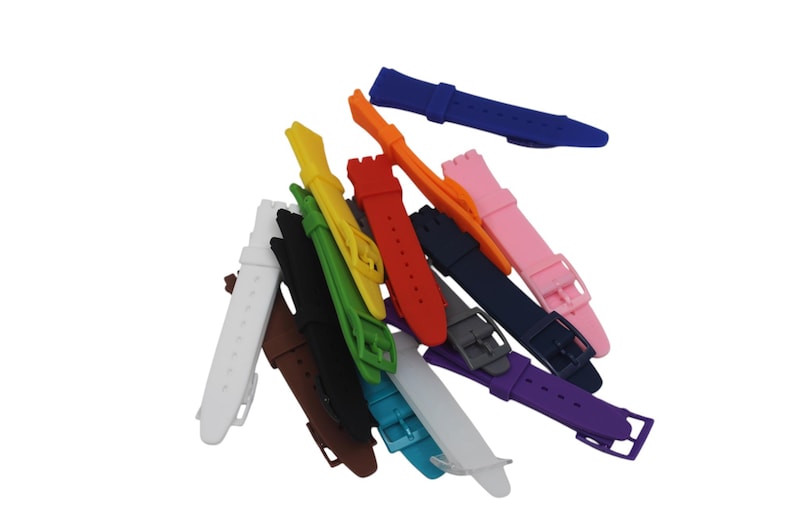 May include: A collection of silicone watch straps in a variety of solid colors including white, brown, black, green, yellow, red, orange, pink, dark blue, gray, purple, and light blue. Each strap features a buckle and multiple adjustment holes.