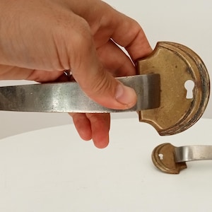 Puede incluir: Un par de manillas de puerta antiguas con acabado en latón y un agujero para llave. Las manillas son de metal y tienen un diseño sencillo.