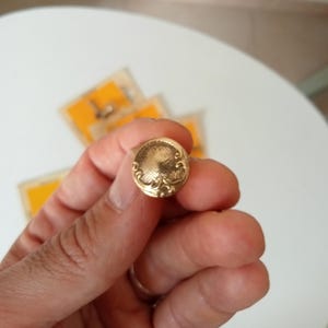 Könnte beinhalten: Ein goldfarbener Ring mit einem runden, verzierten Design. Der Ring wird in einer Hand gehalten.