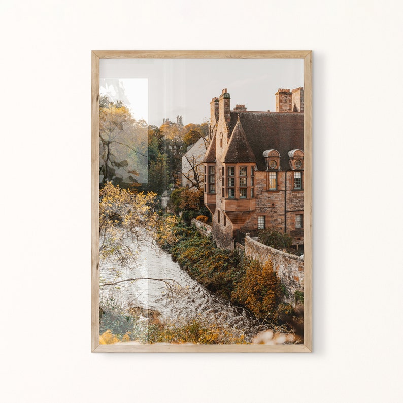 May include: A photograph of a stone building with a river in the foreground. The building is a light brown colour and has a steep roof. The river is flowing through a wooded area. The image is taken from a high angle, looking down at the building and river.