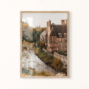 May include: A photograph of a stone building with a river in the foreground. The building is a light brown colour and has a steep roof. The river is flowing through a wooded area. The image is taken from a high angle, looking down at the building and river.