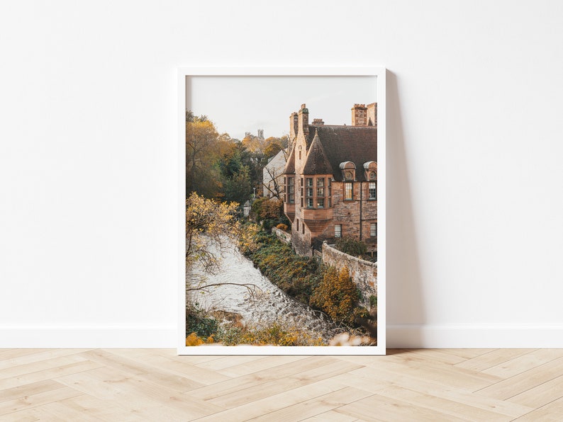 May include: A photograph of a stone building with a brown roof and a small stream in front of it. The building is surrounded by trees with autumn foliage.