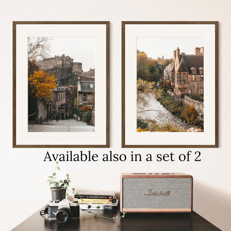 May include: Two framed prints of Edinburgh, Scotland. The first print shows a street lined with buildings and a view of Edinburgh Castle in the distance. The second print shows a view of a stone building with a river in the foreground.
