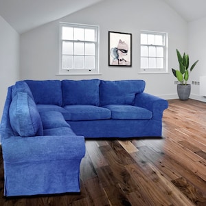 Könnte beinhalten: Ein großes, blaues Ecksofa mit einer Chaiselongue. Das Sofa steht in einem Wohnzimmer mit Holzboden und zwei Fenstern.