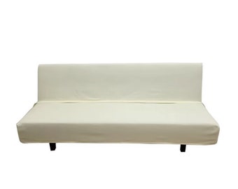 May include: A cream-coloured futon sofa with a simple design. The sofa has a smooth fabric cover and black legs.