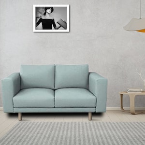 以下が含まれることがあります： 木製の脚が付いた薄い青色の2人掛けソファ。ソファは、グレーの壁の前にあり、その上に白黒の写真が飾られています。
