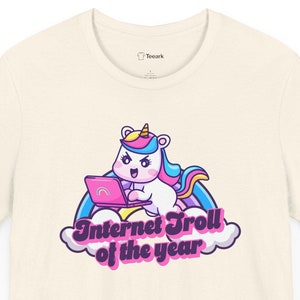 May include: A white t-shirt with a cartoon unicorn wearing a pink shirt and holding a laptop. The unicorn is sitting on a rainbow and clouds. The text "Internet Troll of the year" is printed below the unicorn.