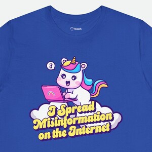 May include: A royal blue t-shirt with a cartoon unicorn using a laptop. The unicorn is pink, blue, and yellow. The text on the shirt reads "I Spread Misinformation on the Internet".