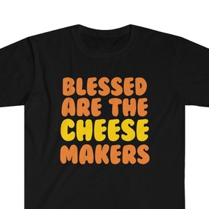 May include: Black t-shirt with the text "Blessed are the cheese makers" in orange and yellow letters.