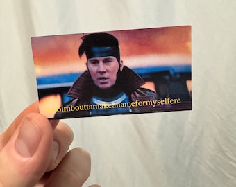 May include: A sticker featuring a man with a black headband and a brown leather jacket. The background is a blurry sunset. The text "imbouttamakanameformyselfe" is printed on the sticker.