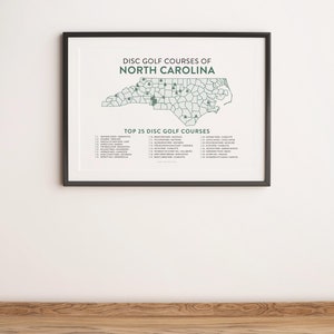 May include: A black framed print with a map of North Carolina highlighting the top 25 disc golf courses. The map is in green and white. The text "Disc Golf Courses of North Carolina" is at the top of the print. The text "Top 25 Disc Golf Courses" is below the map.