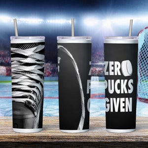 May include: Three stainless steel tumblers with hockey-themed designs. The first tumbler features a black and white image of a hockey skate. The second tumbler has a black background with a white hockey stick and the text "Zero Pucks Given". The third tumbler has a black background with the text "Zero Pucks Given" and a white hockey puck.