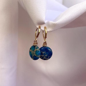 May include: Gold hoop earrings with a blue and white marbled stone pendant.
