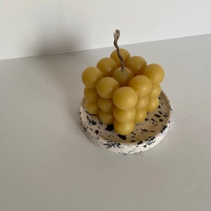 May include: A yellow honeycomb-shaped candle with a wick sits on a white and black speckled ceramic dish.