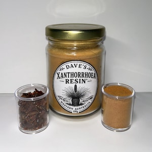 Op de afbeelding: Een glazen pot met Dave's Xanthorrhoea Resin met een gouden deksel, vergezeld van twee kleine doorzichtige containers. Eén bevat donkerbruine stukjes, de andere een fijn, lichtbruin poeder. Het etiket van de pot bevat de tekst "WESTERN AUSTRALIA".
