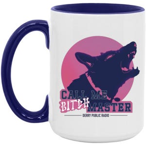 May include: A white ceramic mug with a dark blue handle and interior rim. The front features a graphic of a dark blue howling dog silhouette against a pink circle. Below the dog, the text reads CALL ME BITCH MASTER and DERRY PUBLIC RADIO.