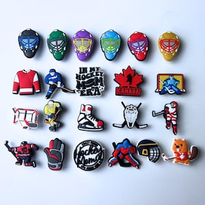 May include: A collection of colorful hockey-themed charms. The charms include goalie masks, jerseys, hockey players, a hockey skate, a hockey net, a maple leaf, and the text "In My Hockey Mom Era" and "Canada".