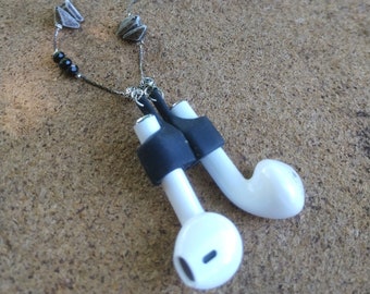 May include: A black and silver necklace with black beads and silver origami-style paper airplanes. The necklace is attached to a pair of white wireless earbuds with black silicone covers.