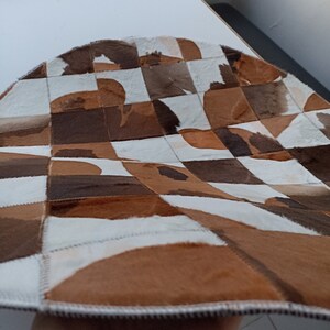 May include: A patchwork rug made of cowhide in shades of brown and white. The rug is made up of squares of different sizes and shapes, and the edges are stitched together.
